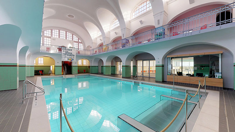 Sicht auf den Eingang zum Schwimmbecken im Jugendstilbad Stadtbad Gotha, pastellfarbige Bogendurchgängen und weiße Kuppeldecke im Stil der 20er Jahre.